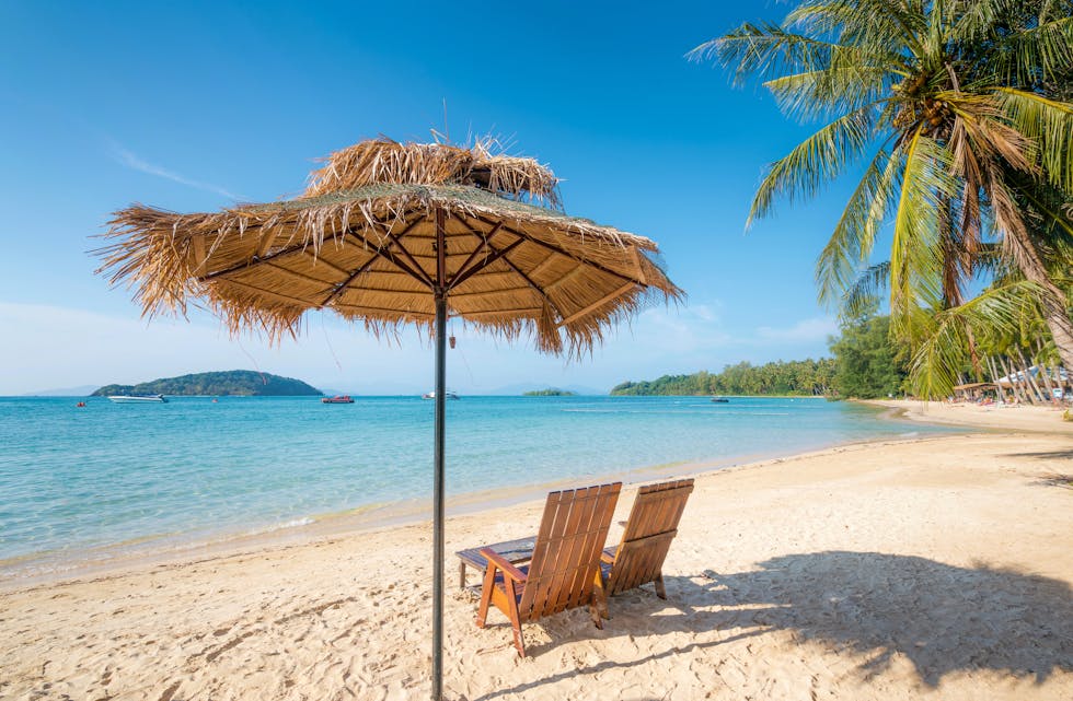Beach Chairs and Umbrella on summer Koh Kood island with clear water sea and wave with speed boat in background in Trat, Thailand. Summer, Travel, Vacation and Holiday concept.